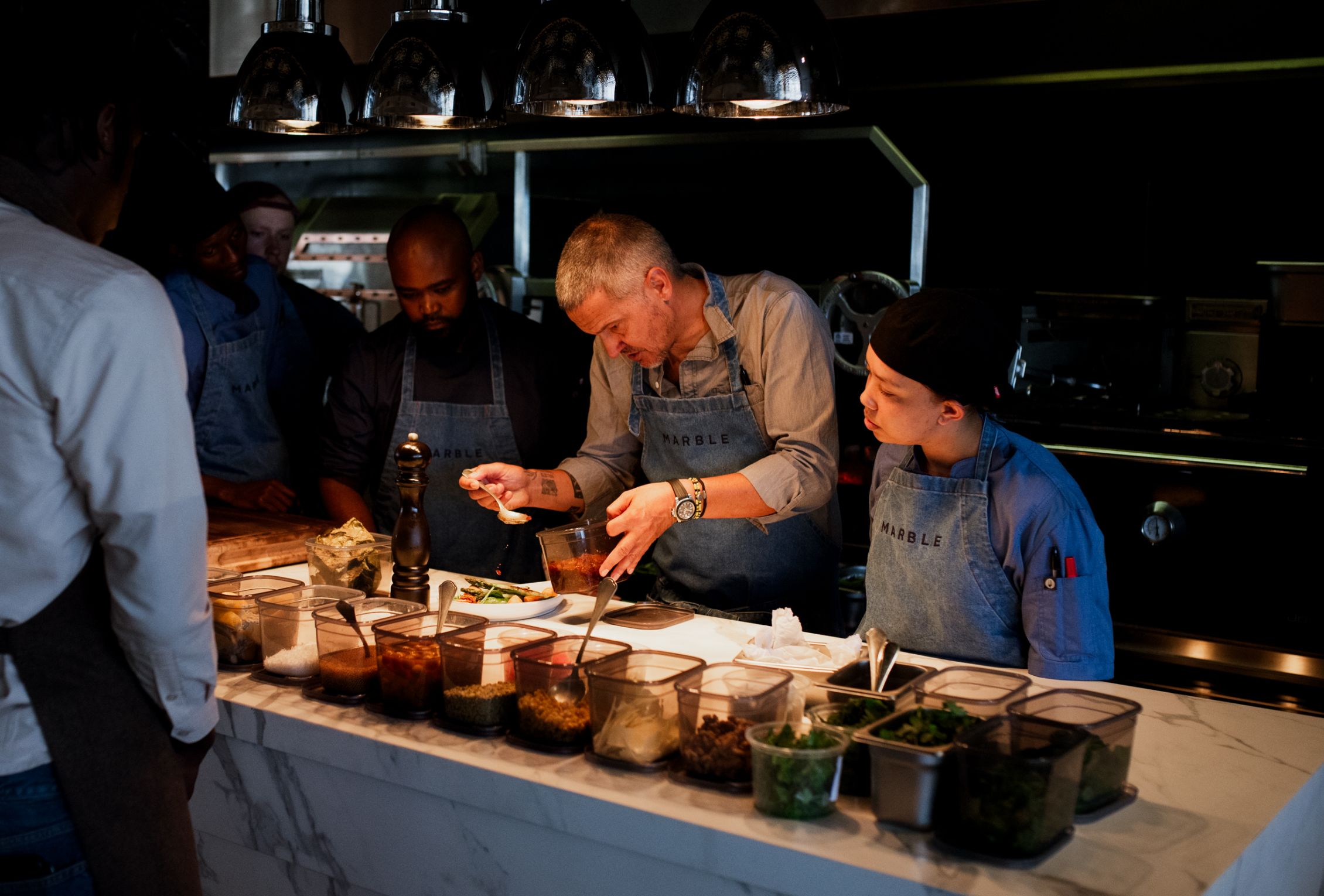 An award-winning chef is seen in an open kitchen, meticulously preparing a dish while surrounded by his team