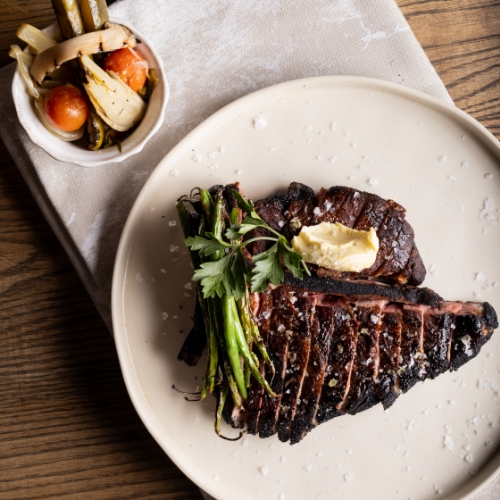 A grilled steak with butter and herbs, alongside green beans and roasted vegetables, a signature item from the steakhouse menu at Marble Restaurant Cape Town