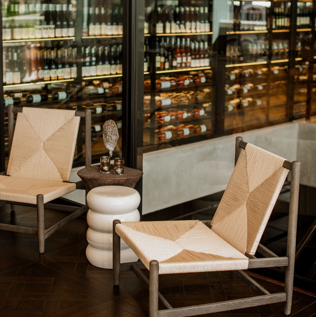 Two stylish chairs are positioned in front of a well-stocked wine cellar, providing a cozy corner within this rooftop bar in Cape Town