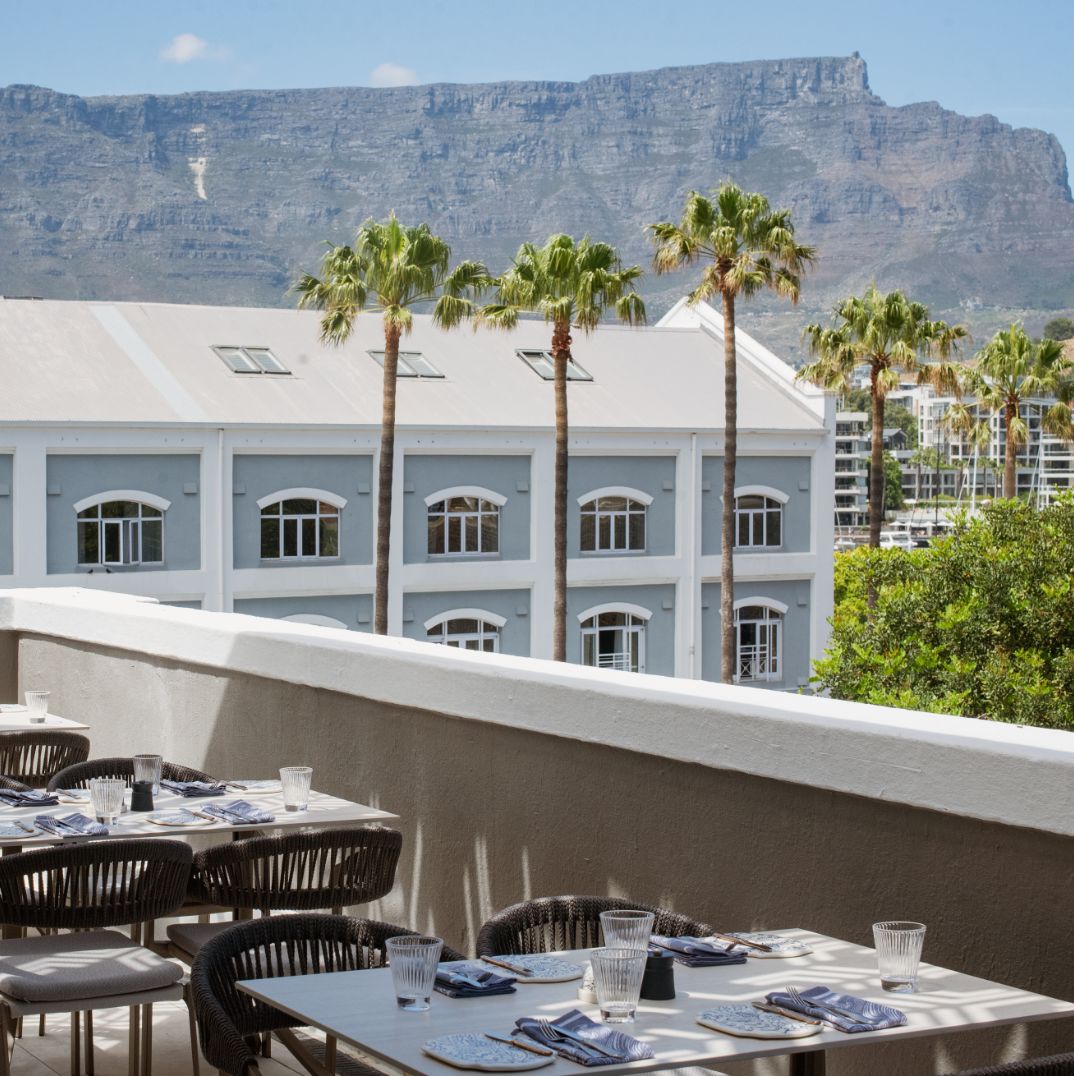 A scenic outdoor terrace at Marble's rooftop bar in Cape Town, featuring set tables and a breathtaking view of Table Mountain and a building with palm trees