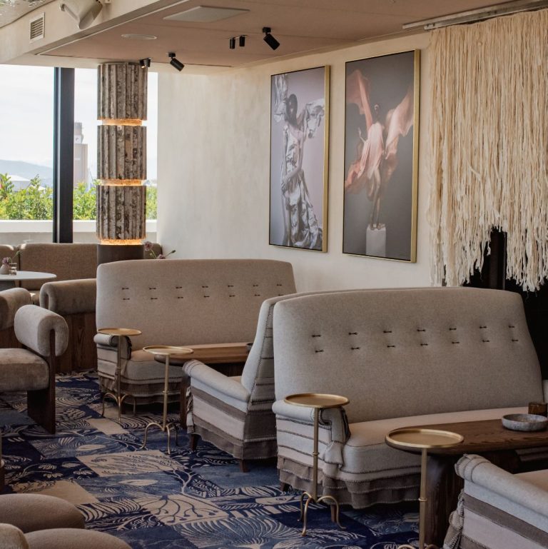 The chic and artistic lounge area of a rooftop bar in Cape Town, with unique furniture, striking artwork, and a detailed patterned rug, creating a sophisticated and comfortable atmosphere