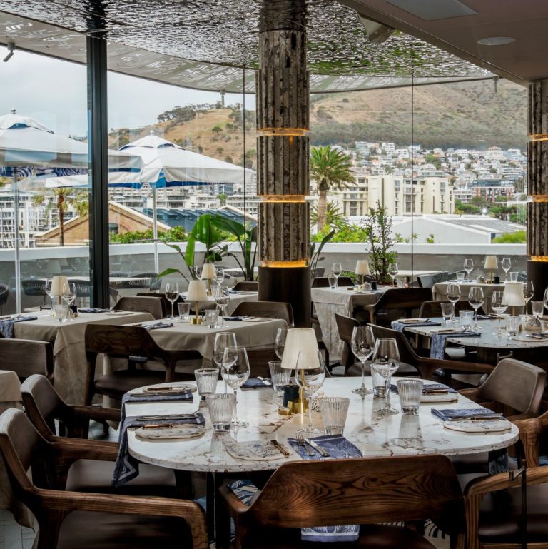 An elegant dining room with a breathtaking view of the city and water, showcasing the ambiance of at Marble's rooftop bar at the V&A Waterfront.