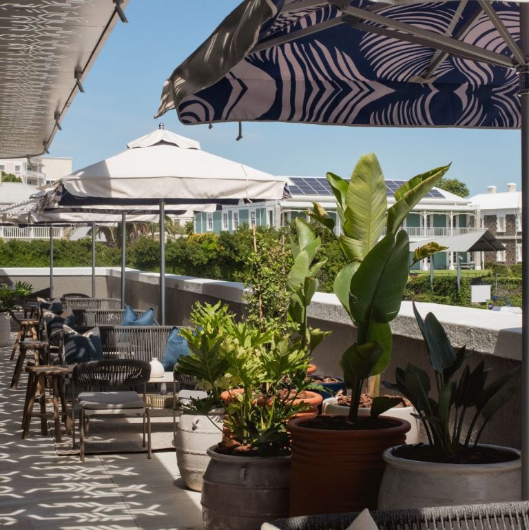 A stylish outdoor terrace with seating and large potted plants, located at a rooftop bar at Marble Restaurant in the V&A Waterfront
