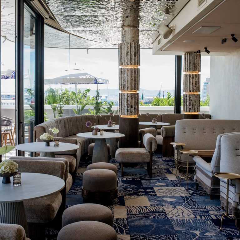The chic lounge at Marble's rooftop bar at the V&A Waterfront, with plush seating and a view of the harbor and outdoor terrace
